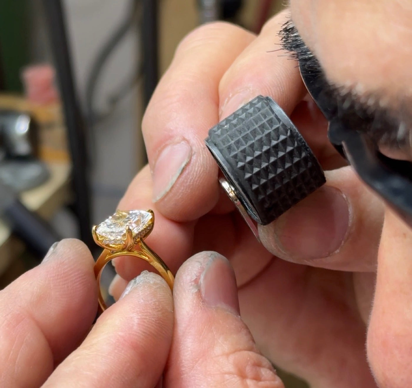 A jeweler inspecting a yellow-gold diamond ring through a loupe at the bench