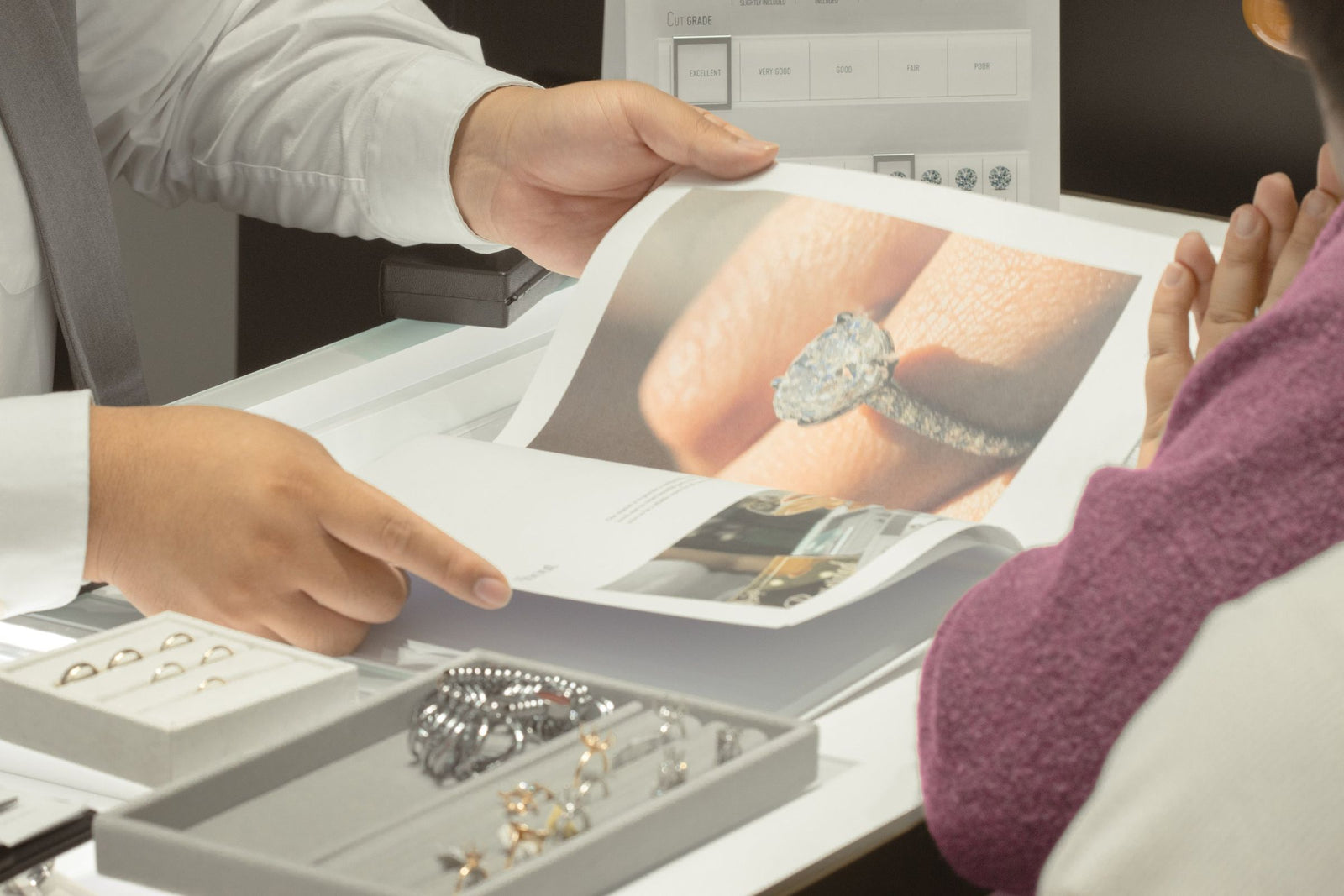 A jeweler showing a client a printed photograph of a pavé oval engagement ring at the consultation counter