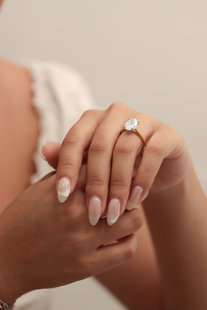 An oval solitaire on a hand with French-tip nails, resting on another hand
