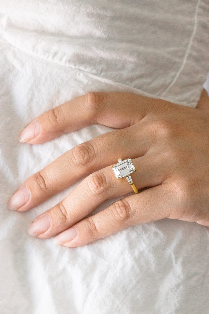 An emerald-cut solitaire on a hand resting on white linen