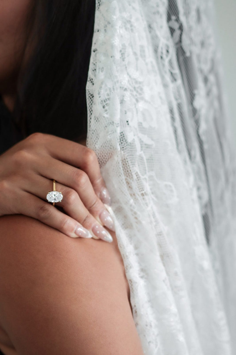 An oval solitaire on a hand resting on a shoulder beside a lace veil