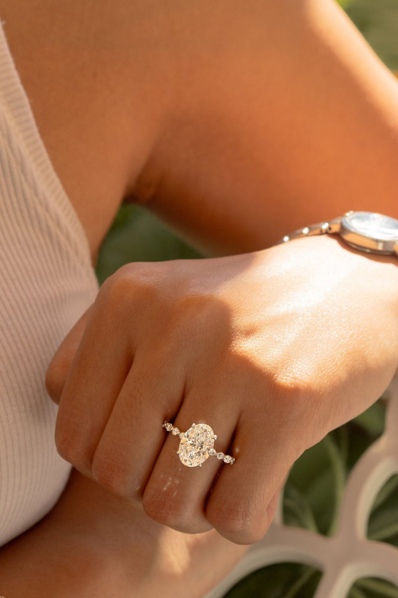 An oval diamond ring on a sunlit hand beside a silver watch