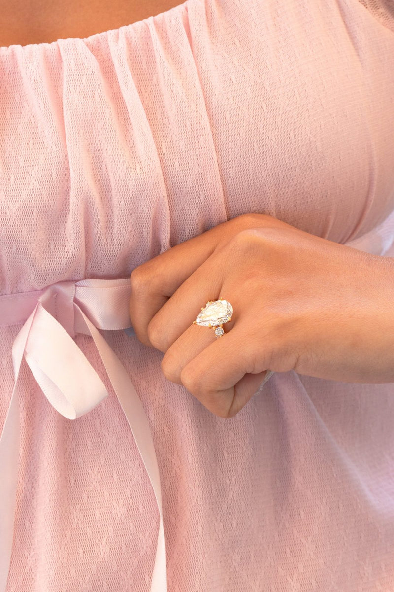 A pear-shaped diamond ring worn against a pink dress with a satin ribbon