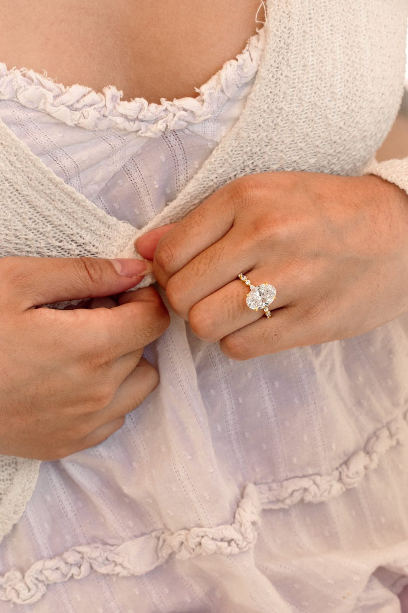 An oval diamond ring on hands gathering a cream cardigan