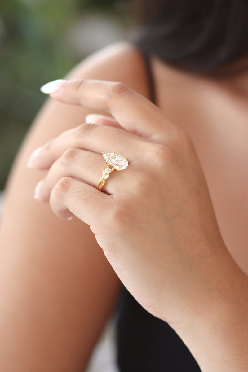 A pear-shaped diamond ring on a hand resting on a shoulder