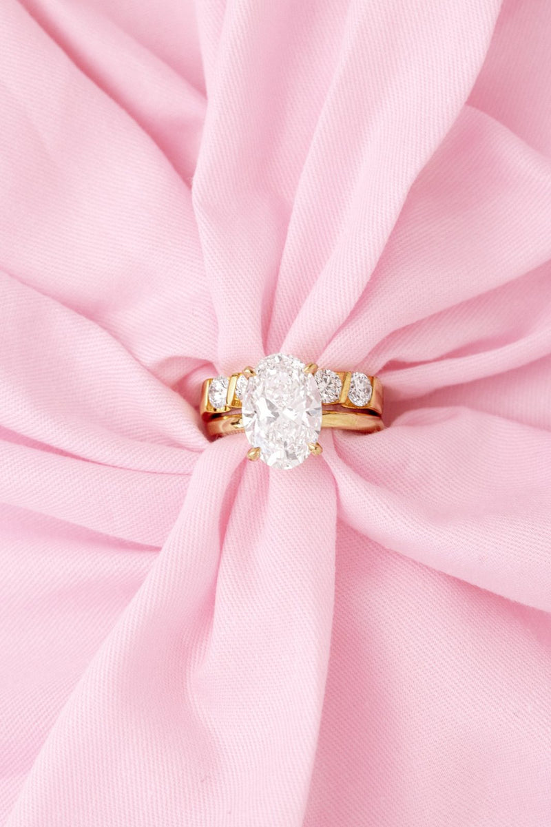 Oval diamond ring with bar-set side stones and a matching band, wrapped in pink fabric