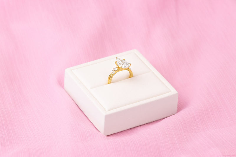 Pear-shaped diamond ring in yellow gold on a white box over pink fabric