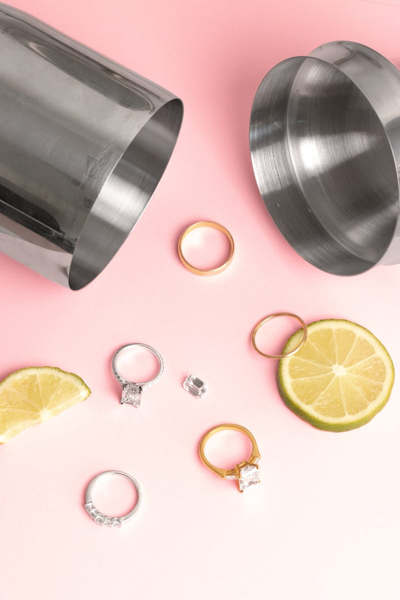 Five rings scattered among lemon slices and steel cups on a pink surface