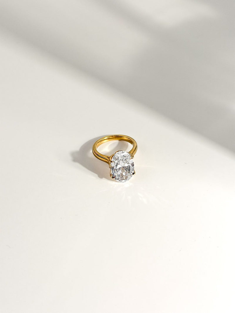 Oval diamond solitaire in yellow gold resting on a white surface