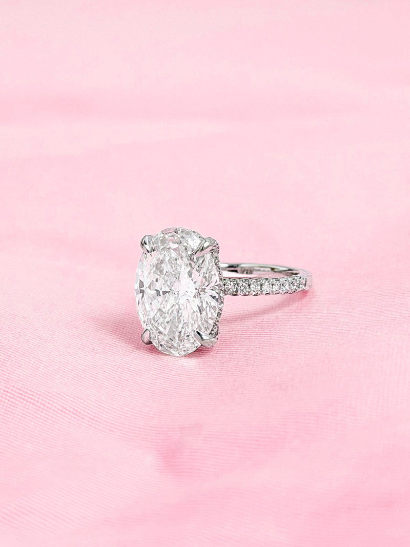 Oval diamond with hidden halo and pavé band in white gold on pink fabric